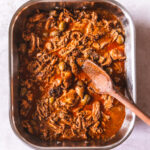 A roaster full of shredded turkey in a red sauce with green olives poking through