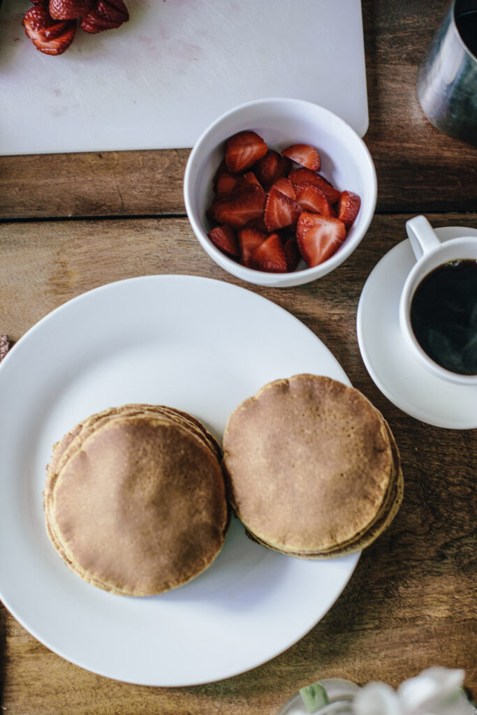 finished pancakes next to coffee and a bowl of sliced strawberries