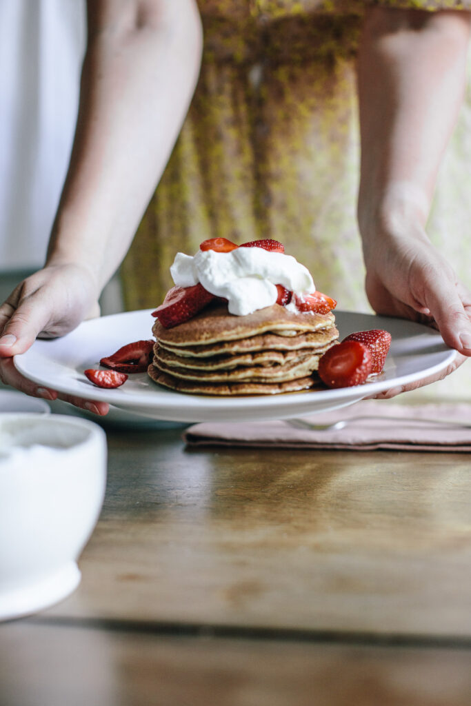 pancake stack with strawberries and whipped cream being held by a female