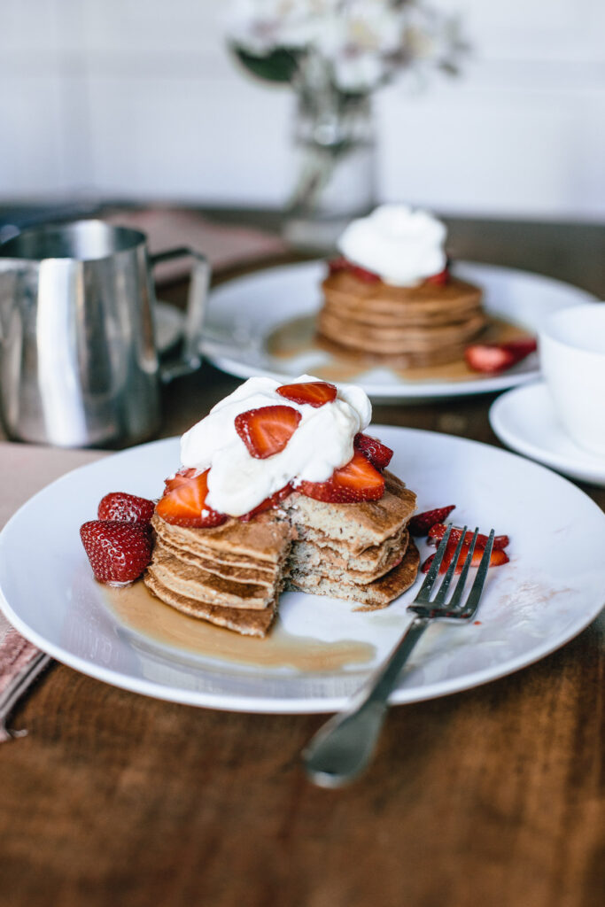 pancake stack with strawberries and whipped cream with a slice taken out of them
