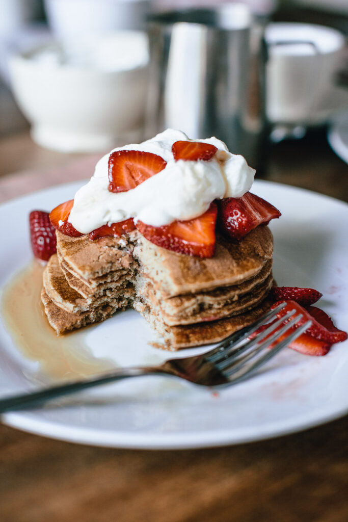 pancake stack with strawberries and whipped cream with a slice taken out of them