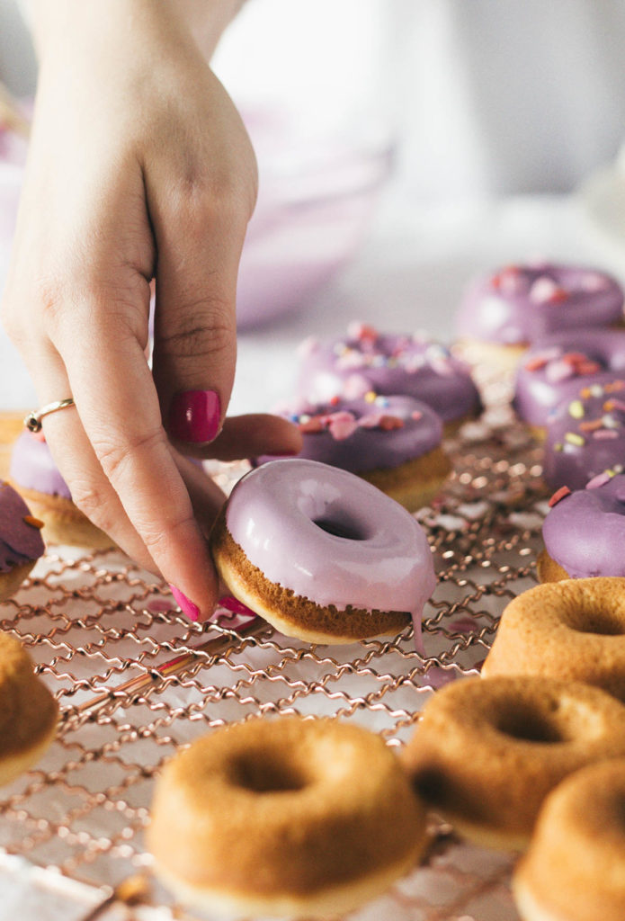 Angled shot of Karlee setting Baked Buttermilk Frosted Mini Donuts on the wire rack. 