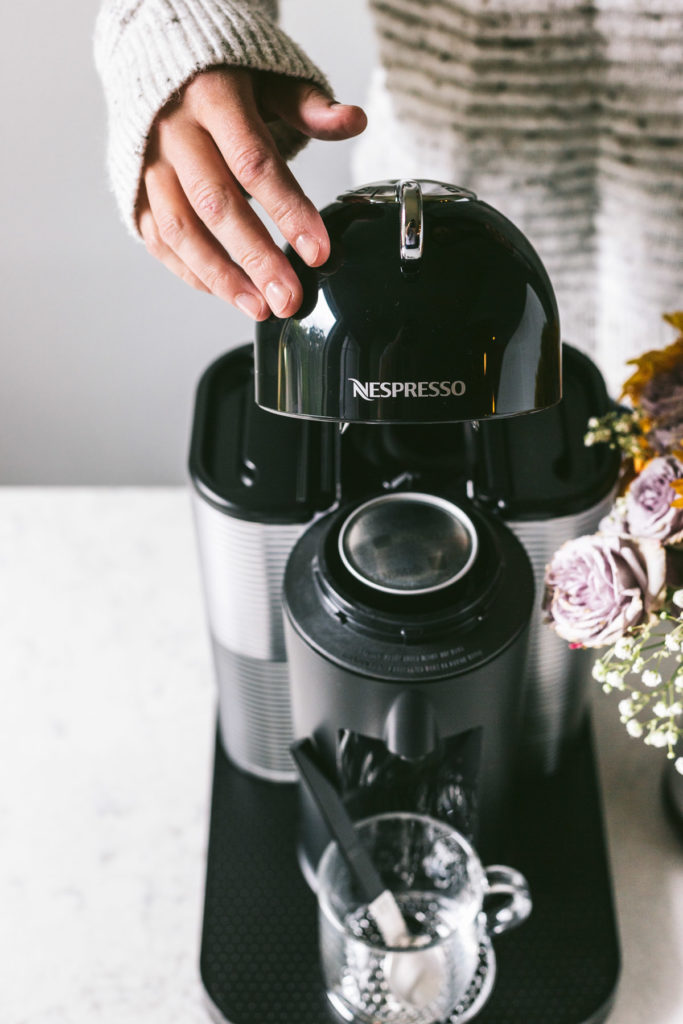 head on image of nespresso machine and a woman behind closing the lid.