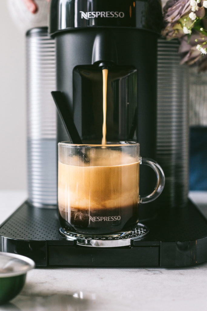 Coffee brewing in the nespresso into a clear cup with lots of top foam