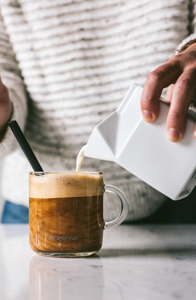 head on image of a woman pouring cream into a clear mug of coffee