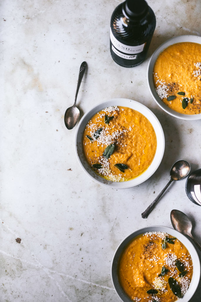 Overhead image of three bowls of butternut squash soup to the right next to vintage spoons