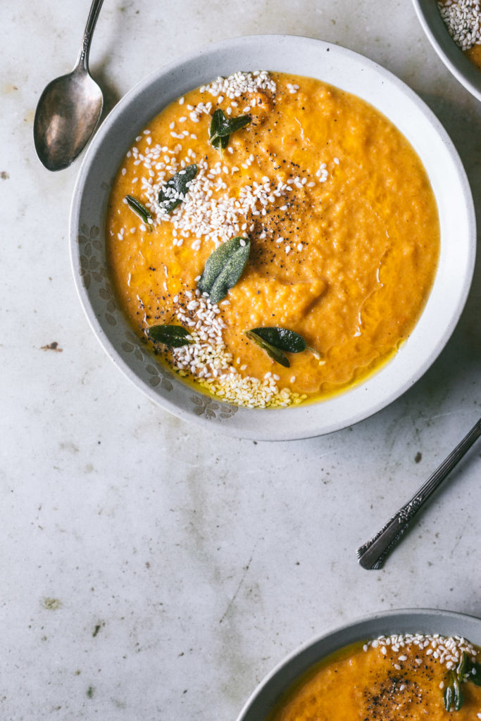 Overhead image of a bowl of butternut squash soup to the right next to vintage spoons