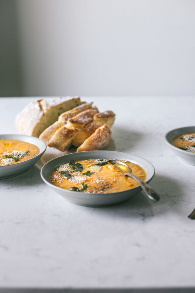 Angled image of butternut squash soup next to a loaf of french bread