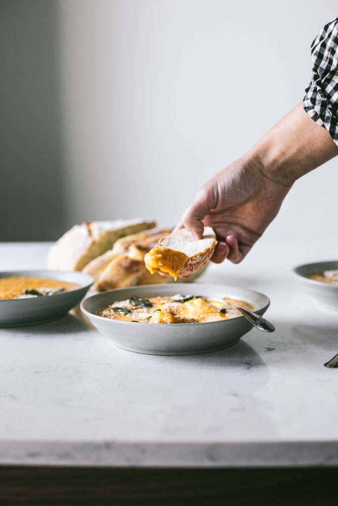 Angled image of butternut squash soup with a slice of french bread dipping into the soup