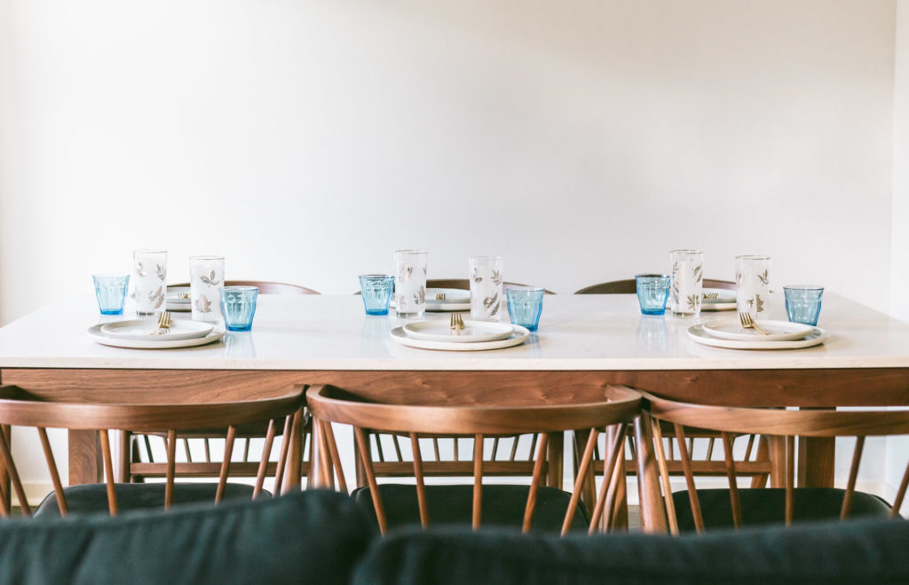 6 place settings with two plates, a gold fork in the middle, a vintage water glass with silver embellishments and a small blue glass next to it.