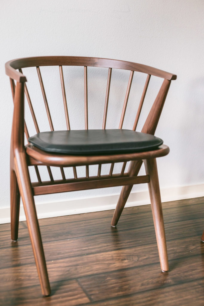 A mid century meets modern chair. Low to the ground. All wood in walnut. Tapered legs. A rounded back with 8 dowels for support. A black, matte leather pad.