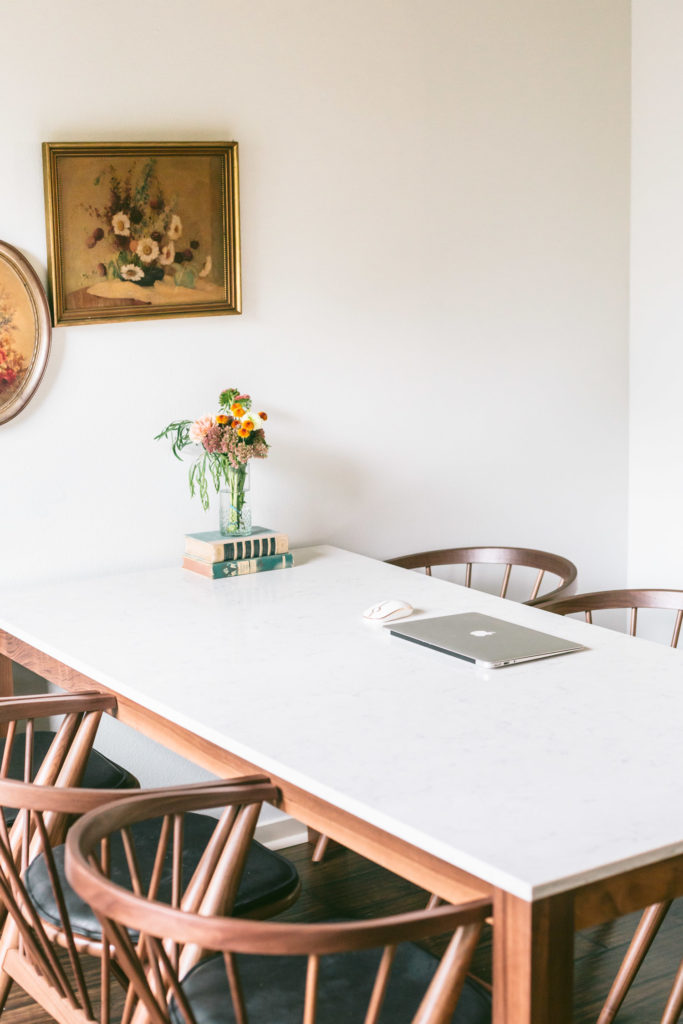 Room & Board dining set with a mac computer and mouse on top. A small floral arrangement sits on vintage books.