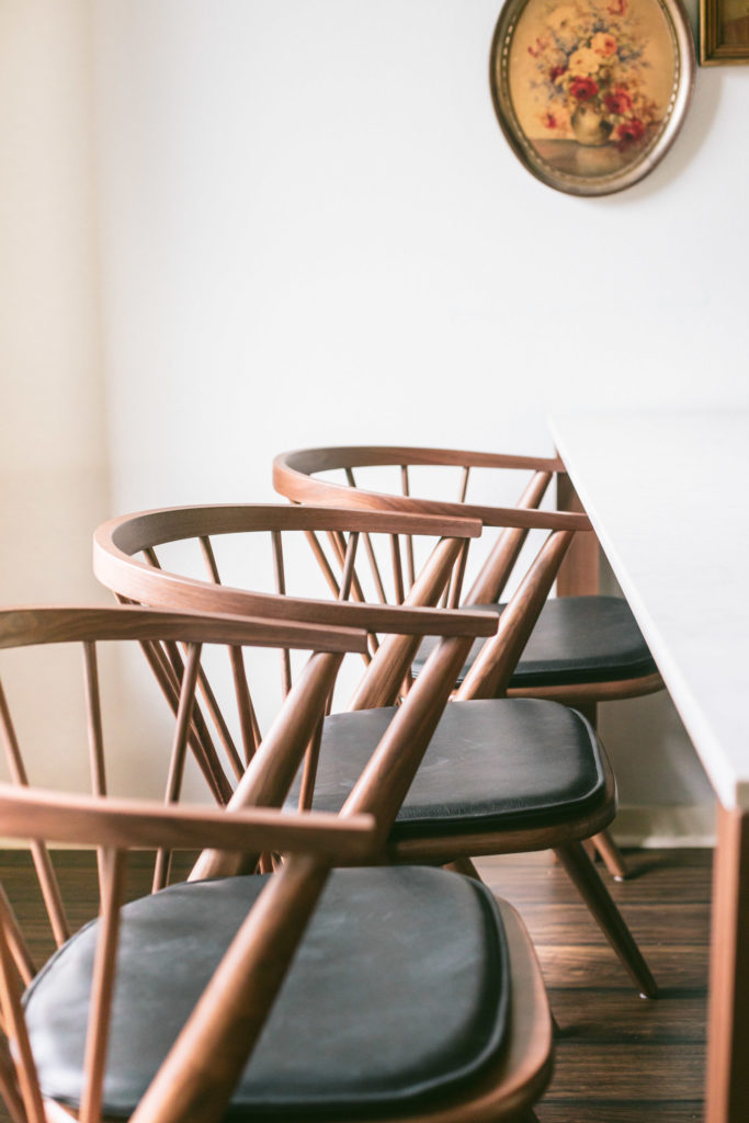 Three mid century meets modern chair. Low to the ground. All wood in walnut. Tapered legs. A rounded back with 8 dowels for support. A black, matte leather pad.