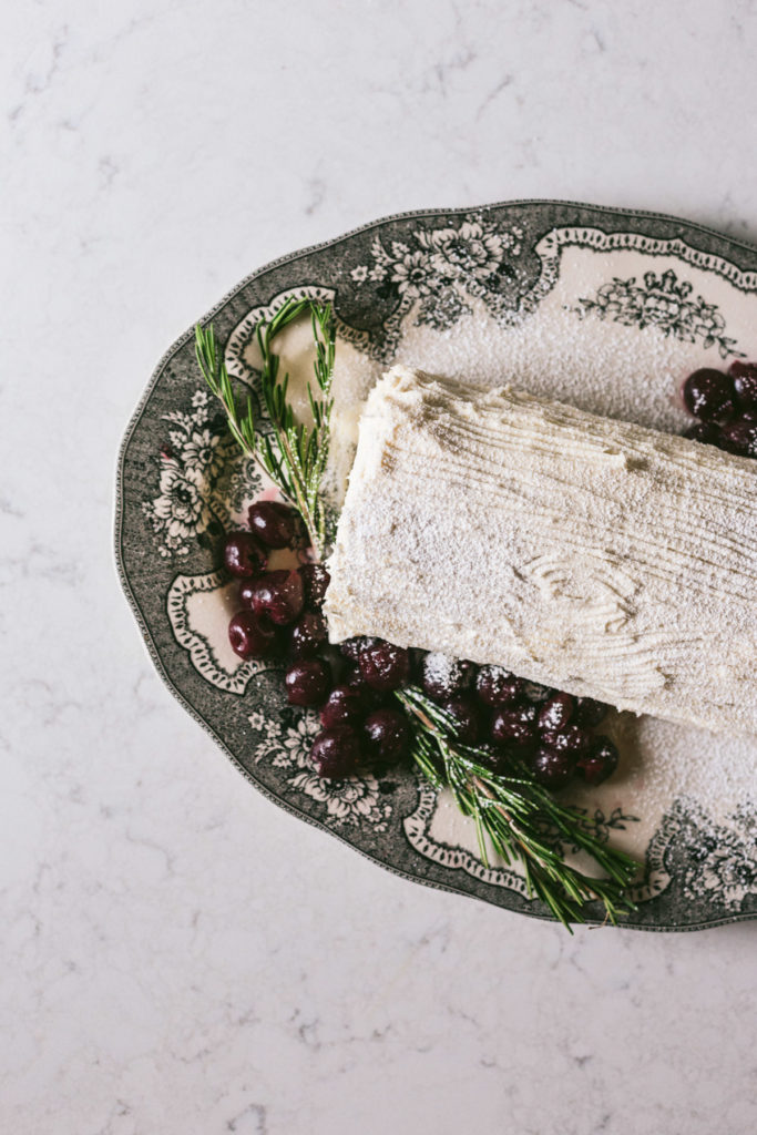 Overhead image of yule log decorated with cherries and rosemary on the side