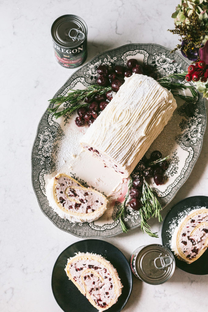 Overhead image of yule log decorated with cherries and rosemary on the side