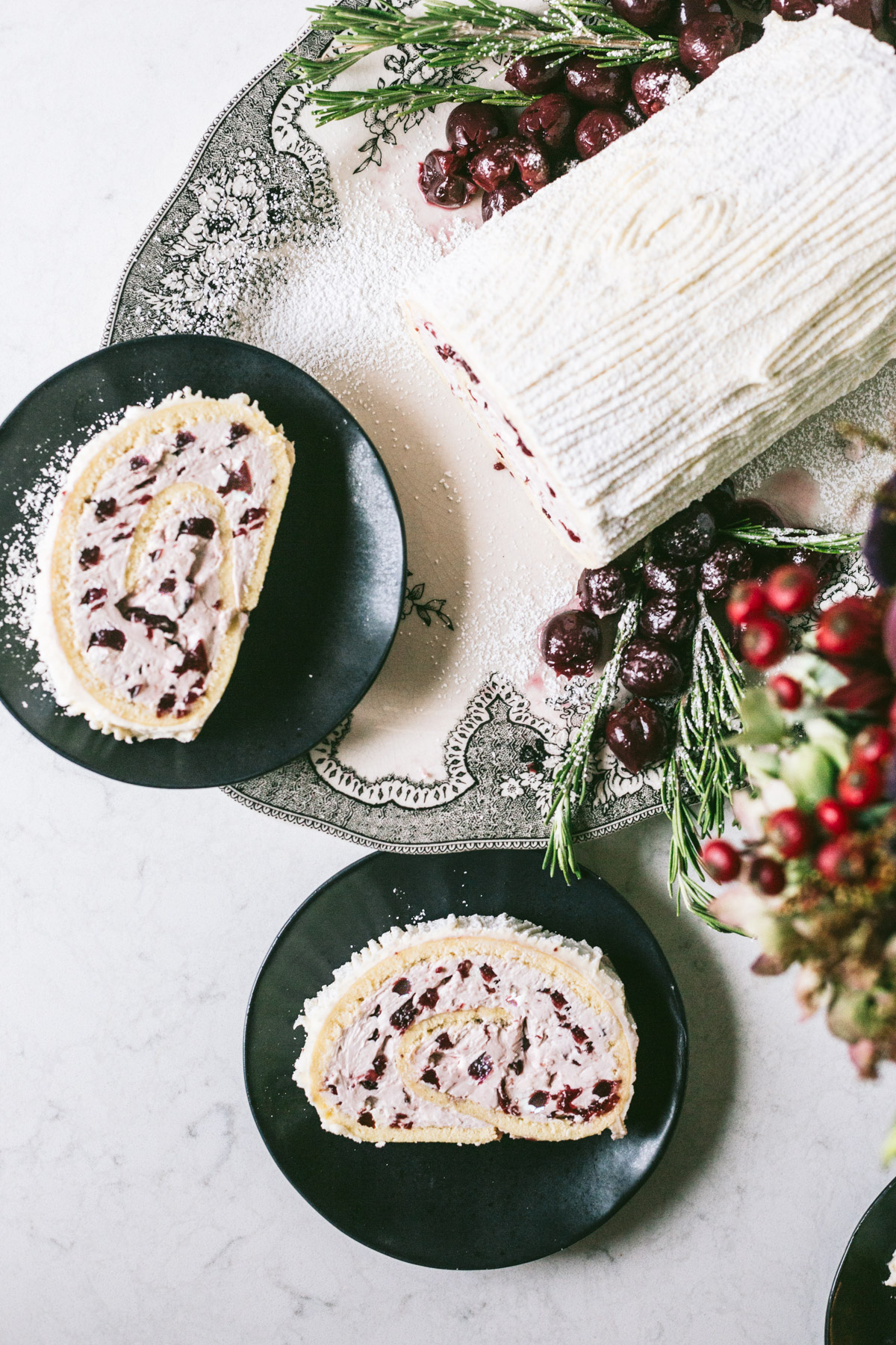 Overhead image of yule log decorated with cherries and rosemary on the side