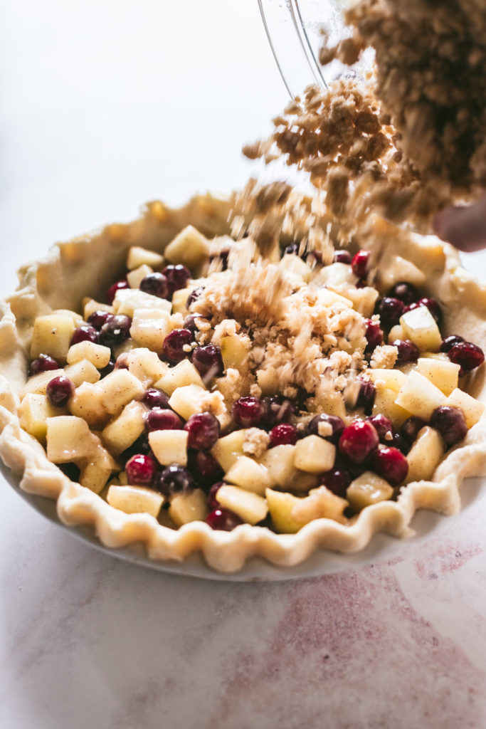 Cranapple pie being topped with crumble