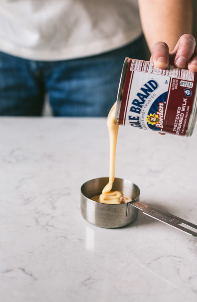 a can of sweetened condensed milk being poured into a measuring cup