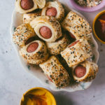 Everything bagel polish dog bites finished and piled in a bowl with condiments on the side