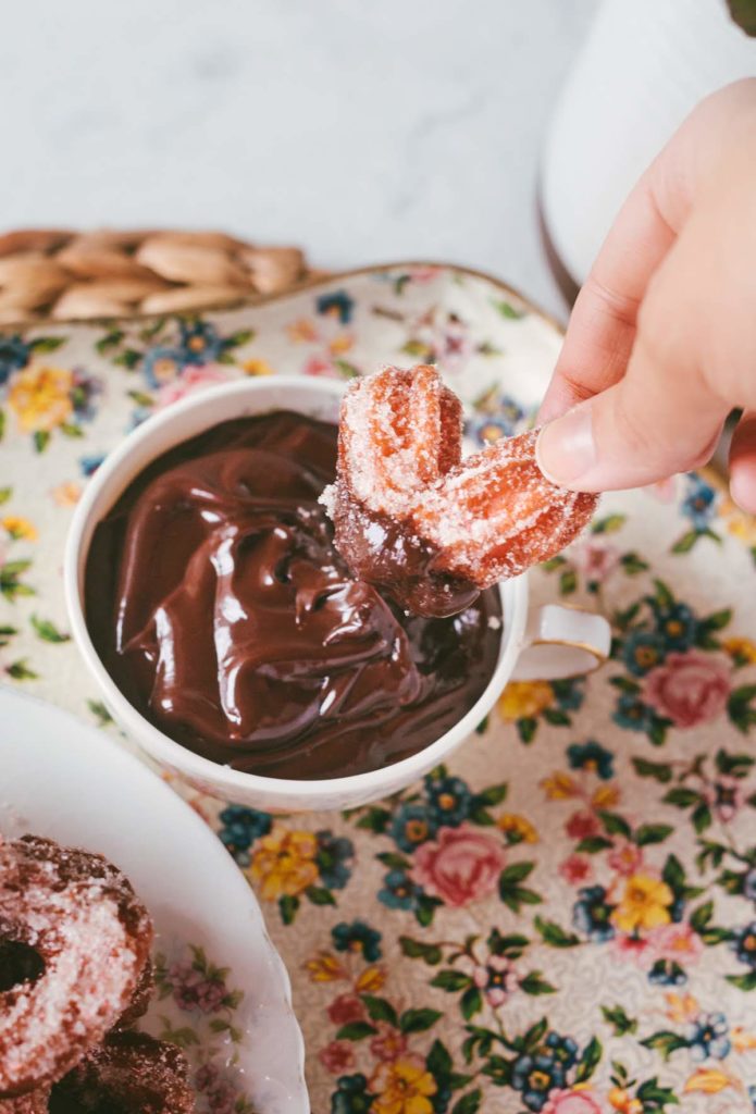 Angled shot of Karlee dipping pink heart-shaped churro into a bowl of shiny ganache.