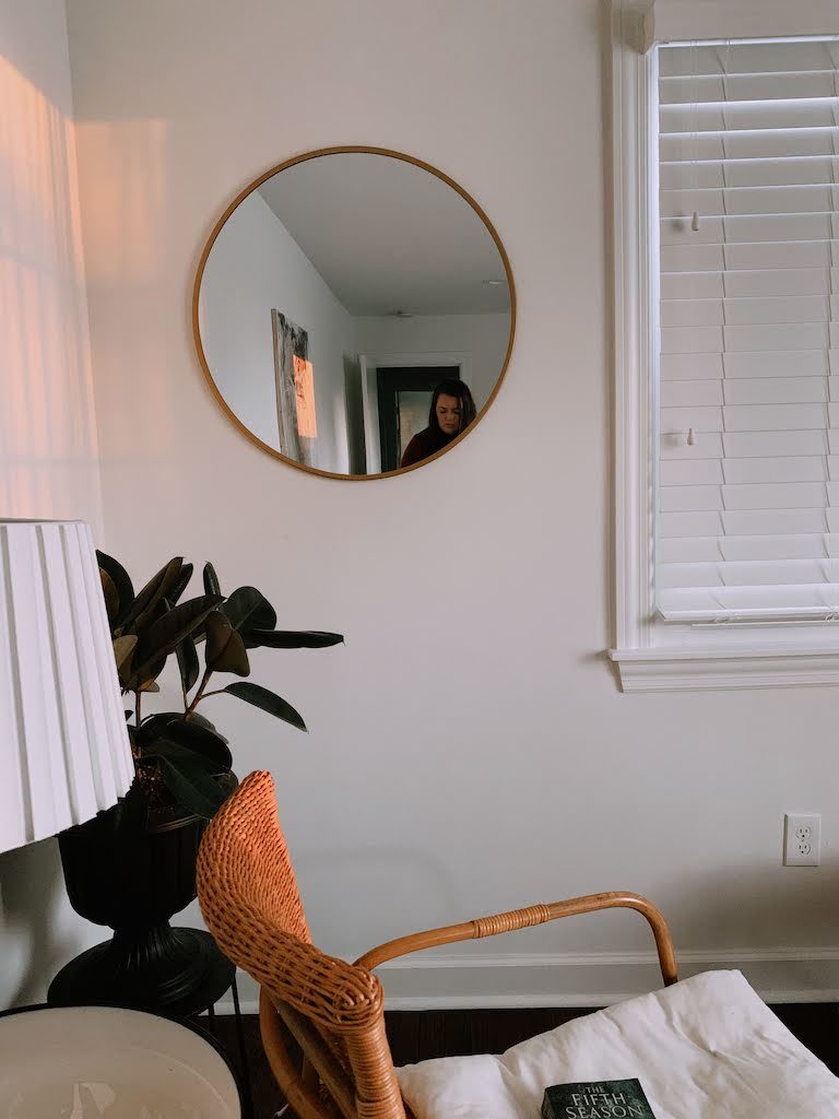 The corner of a room with a chair, mirror and lamp.