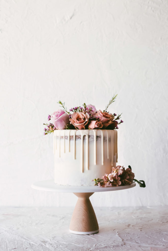 head on image of white cake with white ganache drip and fresh flowers on the top