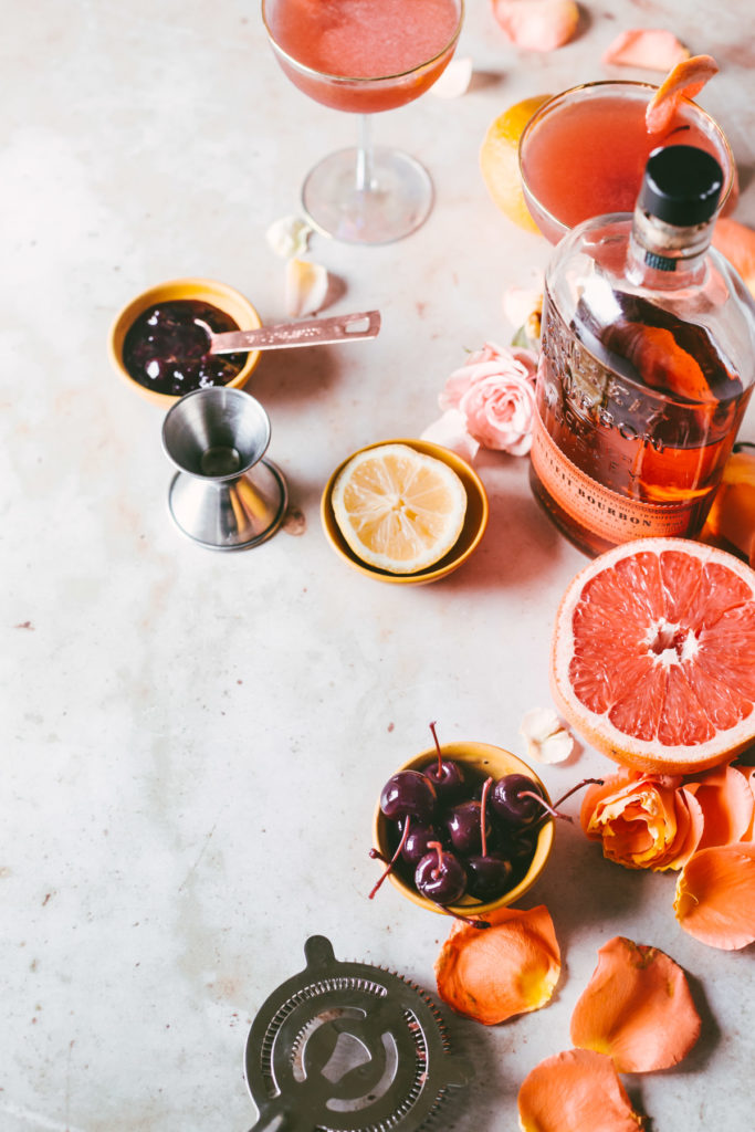 Ingredients for Ruby Bourbon Brown Derby on the table: bourbon, lemon, grapefruit, cherry jam, cherries.