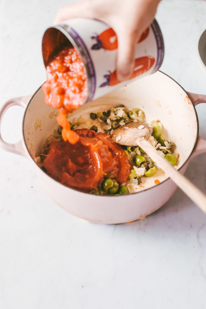 Canned crushed tomatoes being poured into the base of the sauce in a pink cast iron