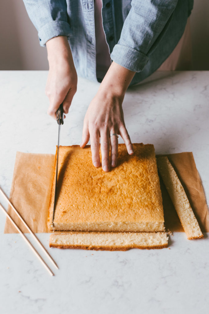 A square yellow cake on a table with edges being cut off