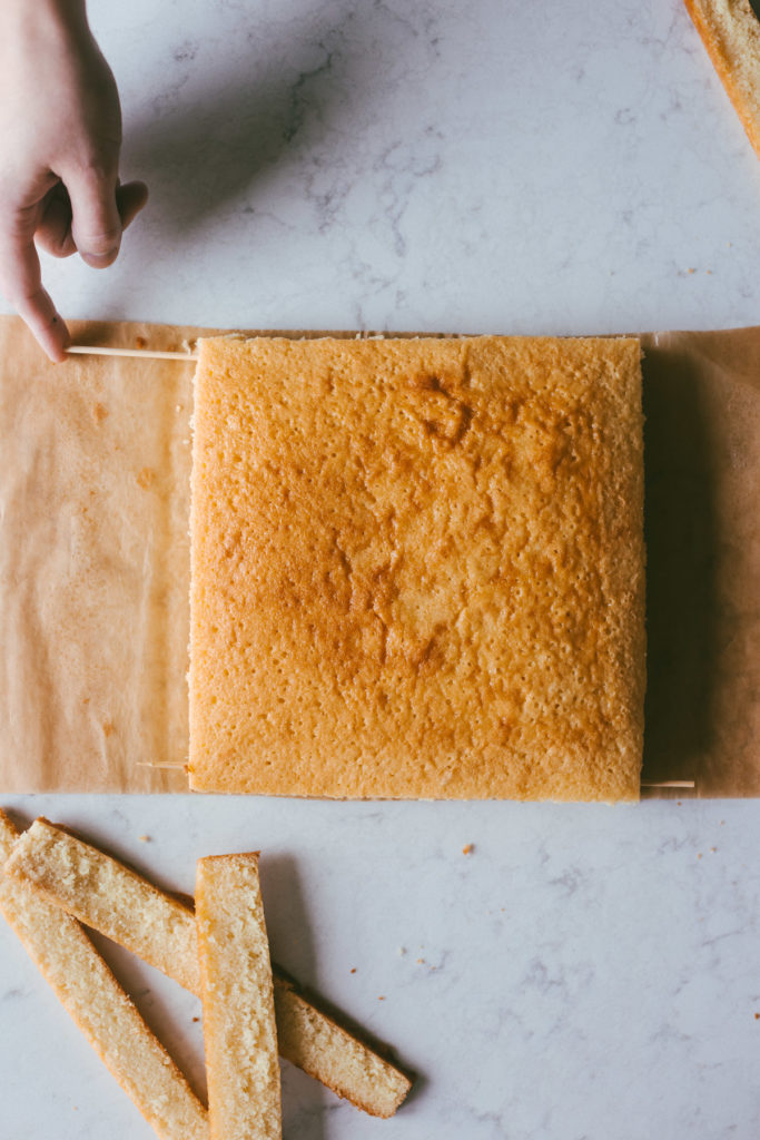 A square yellow cake on a table while skewers are being placed through the center