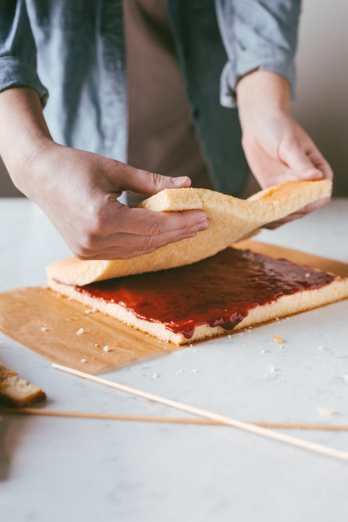 The top of the square yellow cake being placed back onto the bottom of the cake layer with the strawberry filling.