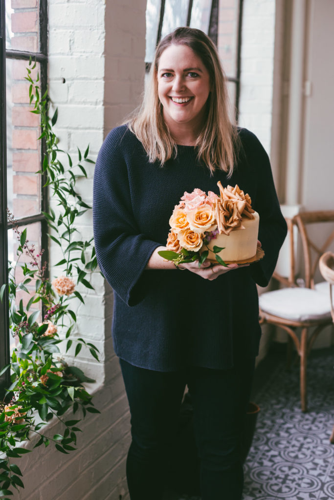 A woman dressed in black holding her decorated cake with fresh flowers
