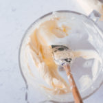 A clear bowl filled with buttercream with a spatula in it