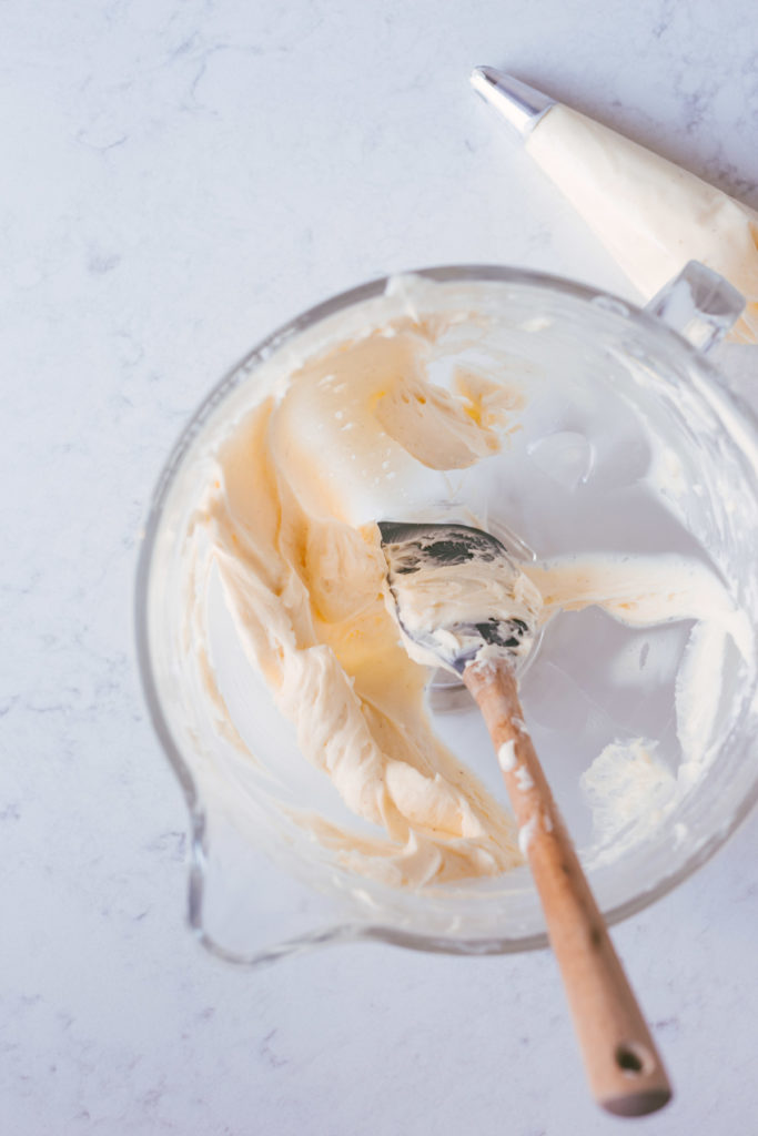 A clear bowl filled with buttercream with a spatula in it