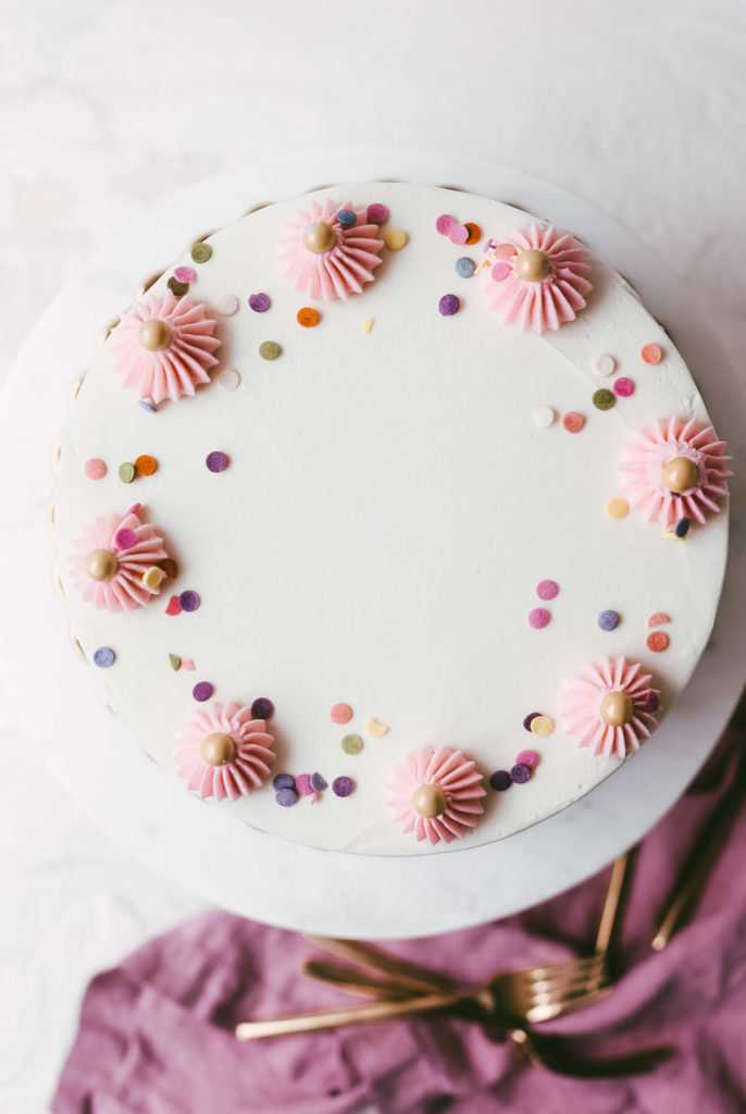 overhead image of a white cake with sprinkles up the sides and pink buttercream dollops on the top