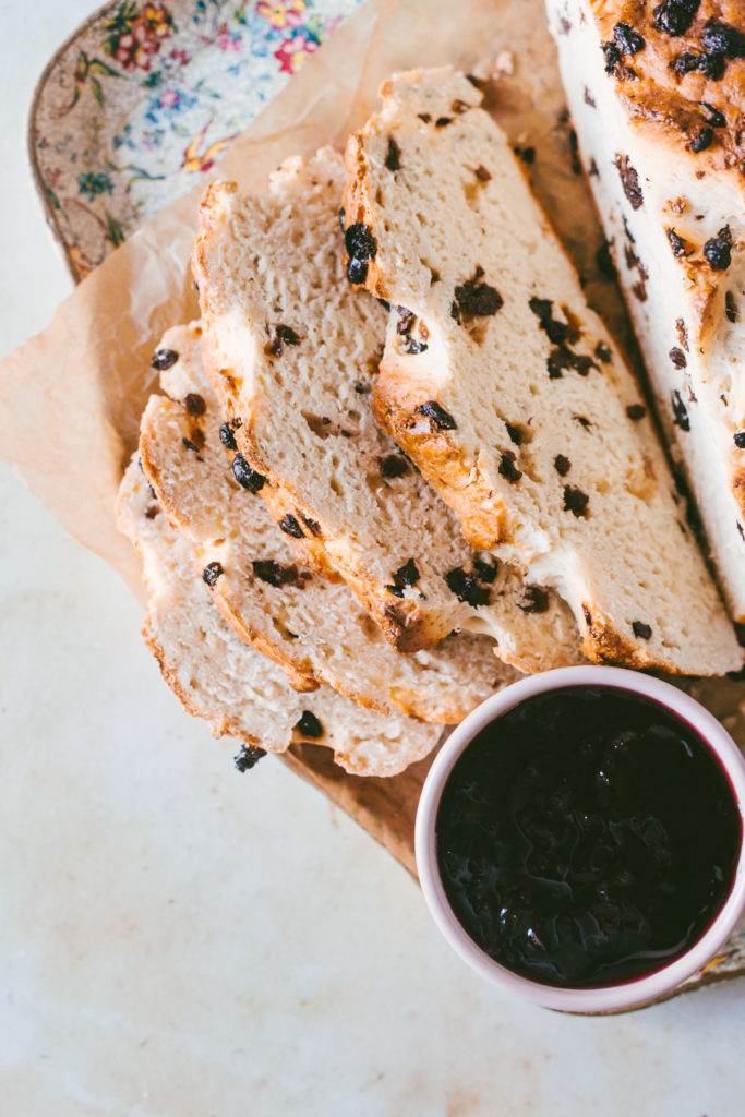 Overhead image of half sliced Irish soda bread laying on a floral try under parchment paper with jam on the side