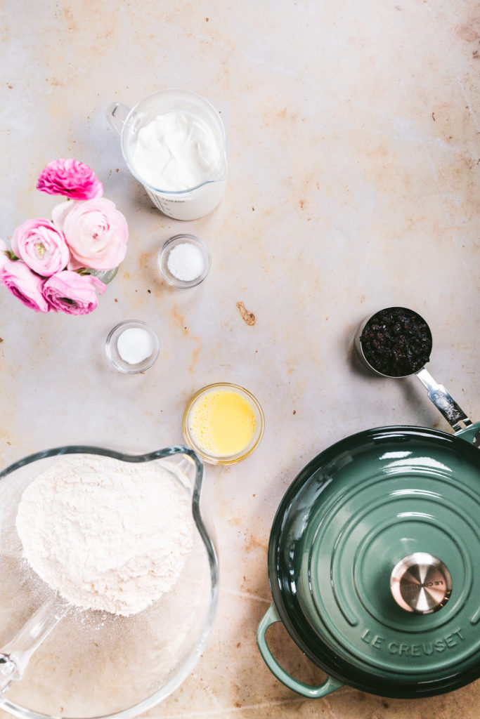 Overhead ingredients shot: baking soda, salt, greek yogurt, currants, flour, egg wash, and green colored le creuset 