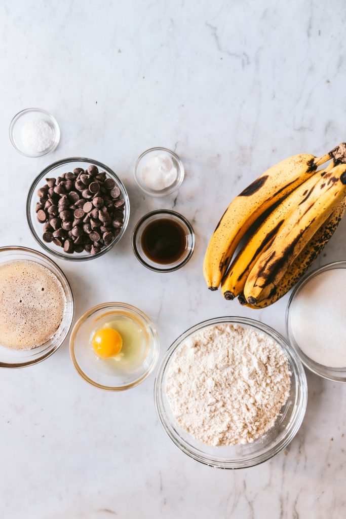 Overhead image of ingredients laid out on the table. Ripe bananas, egg, vanilla, flour, browned butter, sugar, chocolate chips etc.