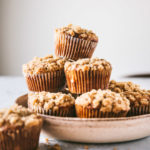 Head on image of browned butter banana chocolate chip muffins stacked in a bowl with a few scattered around it