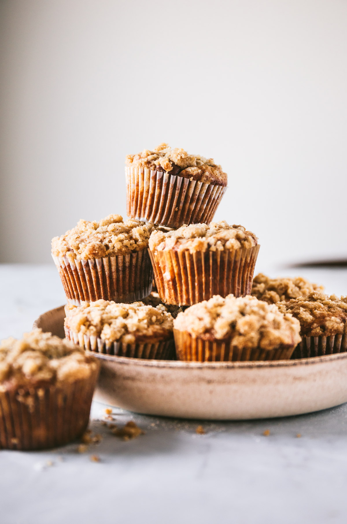 Head on image of browned butter banana chocolate chip muffins stacked in a bowl with a few scattered around it