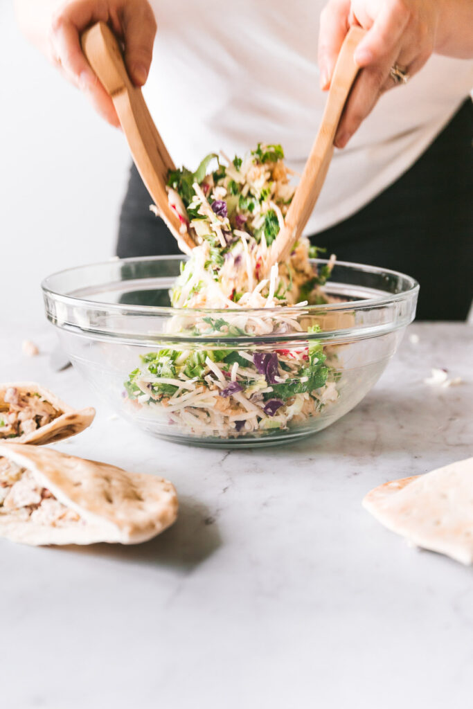 Dill pickle salad being tossed in a glass bowl