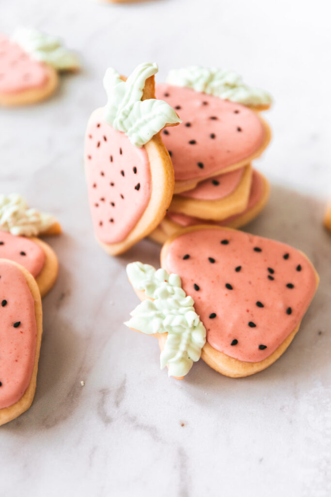 Overhead picture of strawberry shaped cookies with pink icing, black sesame seed decorations and green frosting leaves