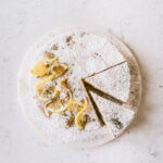 Overhead image of the finished cake with powdered sugar and lemon slices for detail with two slices taken out