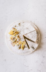 Overhead image of the finished cake with powdered sugar and lemon slices for detail with two slices taken out