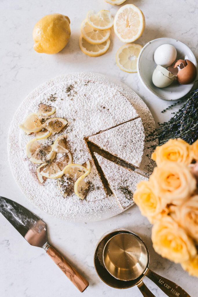Overhead image of the finished cake with powdered sugar and lemon slices for detail. Styled with yellow roses, fresh lavender, empty colored egg shells