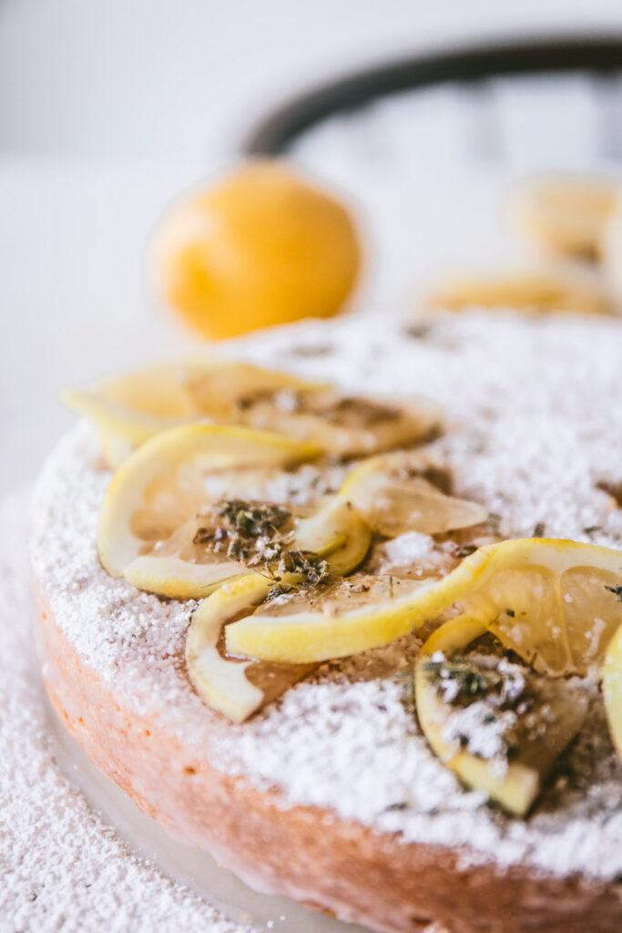 Close up detail of the lemon slices and dried lavender detail on the top of the Head on angle of cake with a slice slightly moved away from the cake