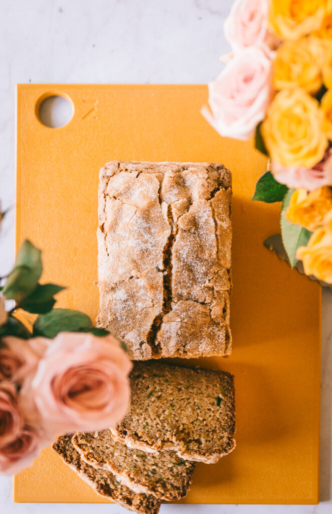 zucchini bread with a few slices taken out and pink and yellow roses on the side