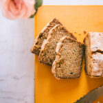 zucchini bread with a few slices taken out and pink and yellow roses on the side