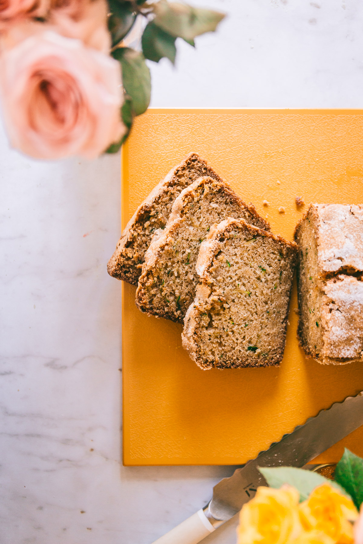 zucchini bread with a few slices taken out and pink and yellow roses on the side