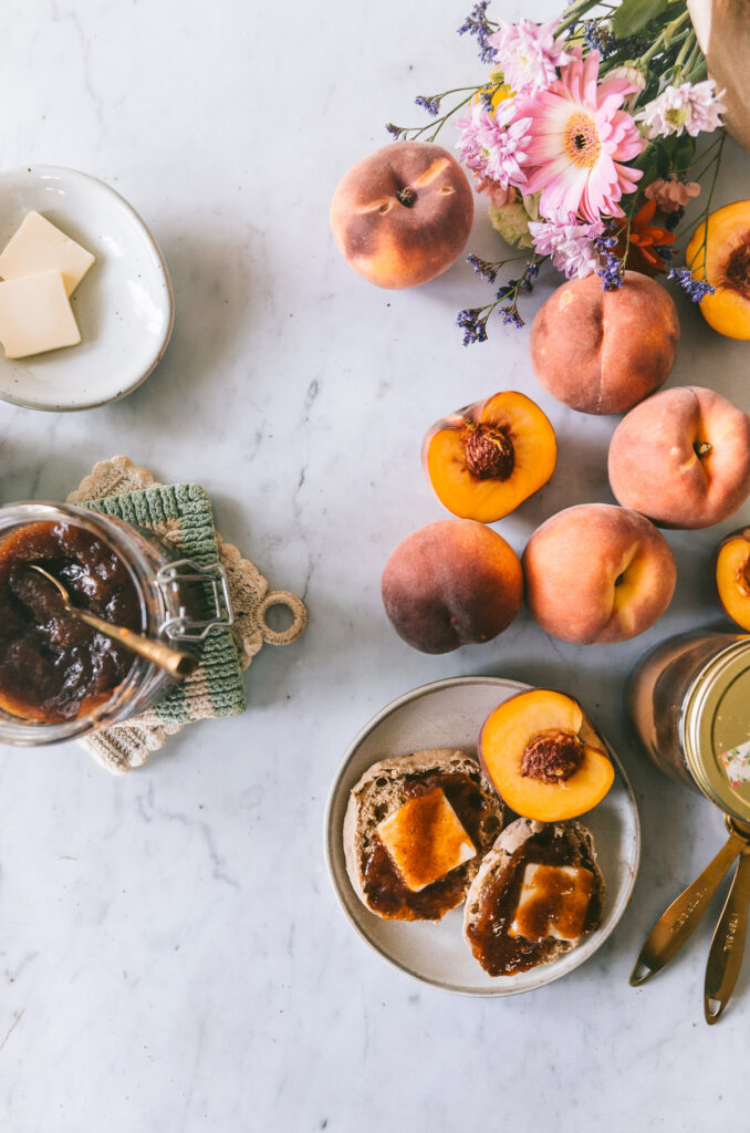 an overhead image with peaches laid out over the table, a open jar of peach butter and an english muffin slathered in peach butter.